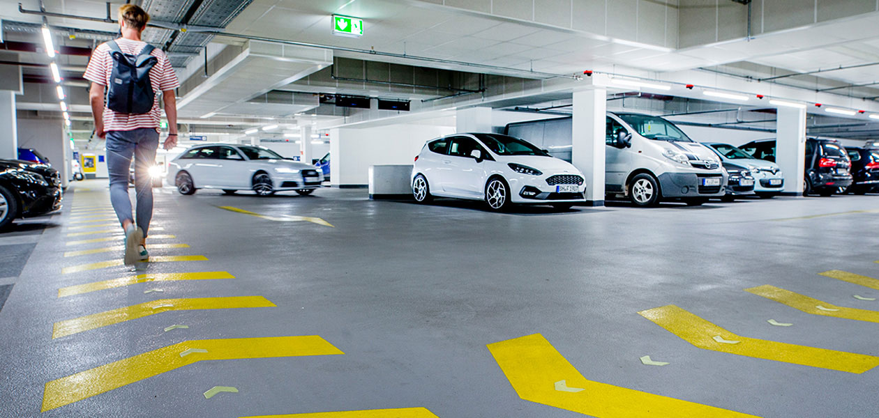 Fußgänger mit Rucksack auf einem gelb markierten Fußweg im Parkhaus