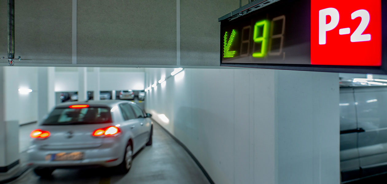 Digitale Anzeigetafel zu freien Parkplätzen auf Parkebene 2 mit verschwommenem Auto im Hintergrund